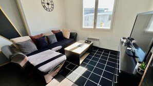 A modern living room with a sofa, a coffee table, a TV, and a large window. - One-Bedroom Apartment – Saint-Éloi, Poitiers (Poitiers)
