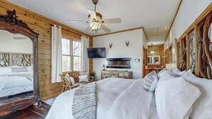 Une chambre confortable avec un grand lit, un ventilateur de plafond en bois, une cheminée et un téléviseur.
