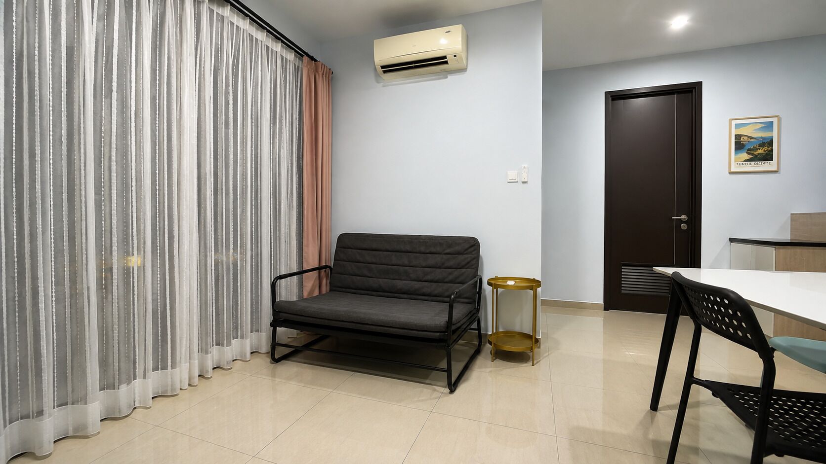 Une pièce comprenant un canapé, une petite table ronde, une chaise, une porte et un appareil de climatisation fixé au mur.