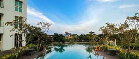 A swimming pool with a clear blue water surface, surrounded by greenery and a modern building.
