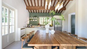 A spacious dining area with a long wooden table and multiple chairs, a kitchen in the background, and a large window providing natural light. - Villa La Pace near Lucca (Province of Pistoia)