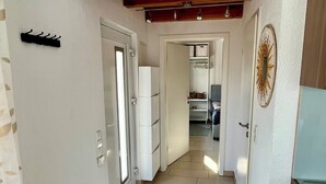 A narrow hallway with a tiled floor, a wooden ceiling, and a white door at the end.