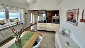 A modern kitchen with stainless steel appliances, a dining area with a wooden table, and a view of the sea through large windows.