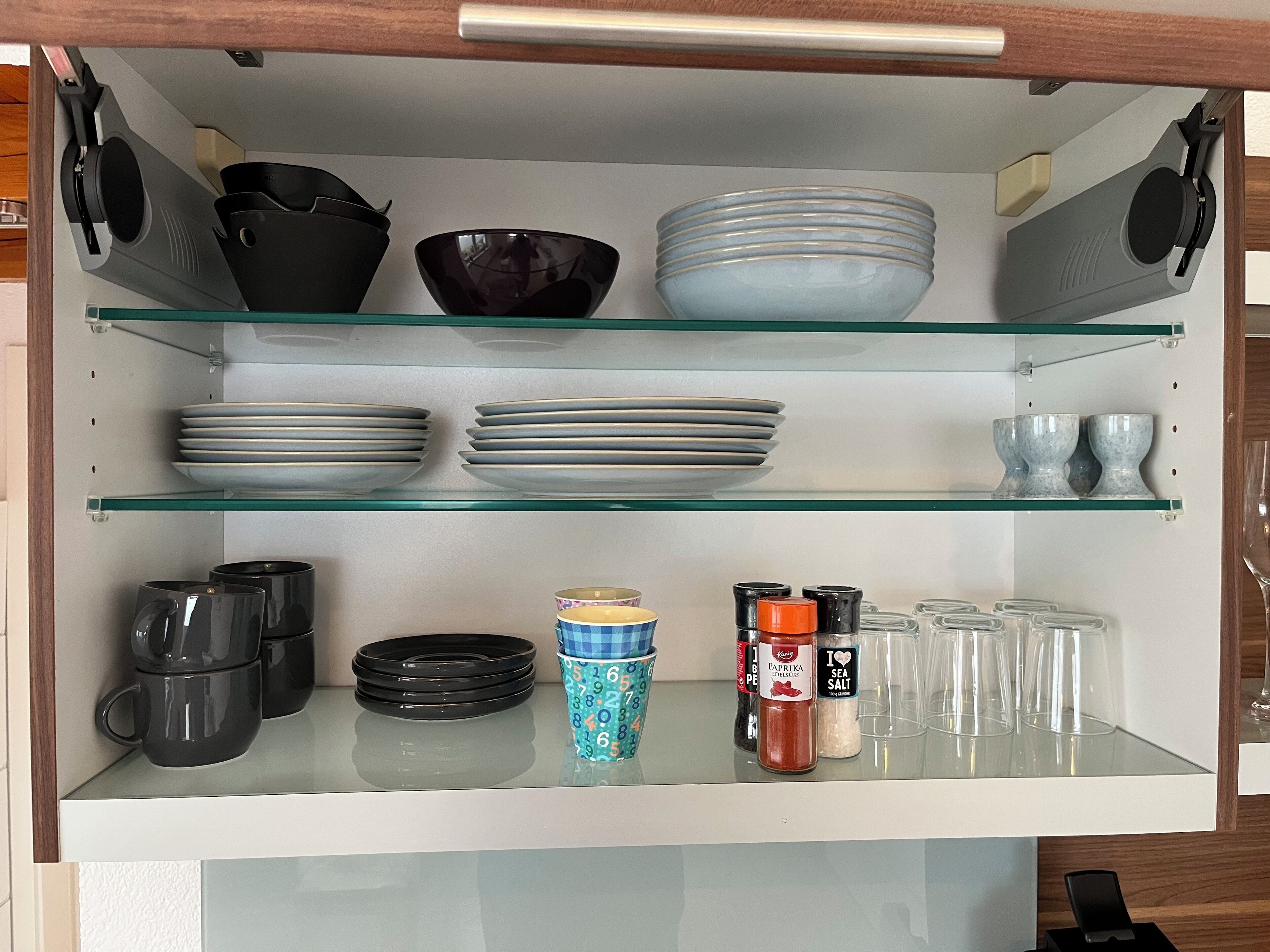 Ett kök med hyllor av glas där tallrikar, skålar och koppar förvaras.