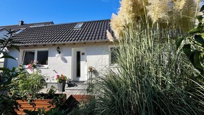 A house with a tiled roof, a white door, and a window. There is a large plant with tall, feathery leaves in the foreground.