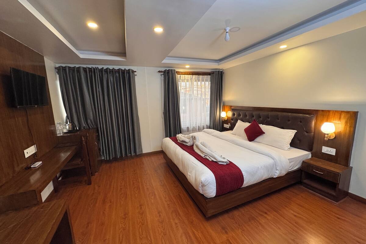 A hotel room with a large bed, wooden flooring, a desk, and a TV mounted on the wall.