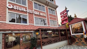 A hotel with a sign reading "STUPA BOUTIQUE HOTEL" and a signboard listing amenities like a seminar hall, terrace bar, lounge, and spa & gym.