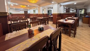 A spacious restaurant with wooden tables and chairs, a central bar area, and decorative lighting fixtures.