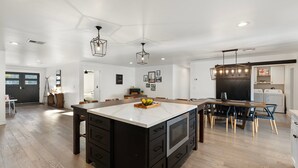 Een ruime keuken met een groot kookeiland, moderne hanglampen en een eethoek met houten stoelen.