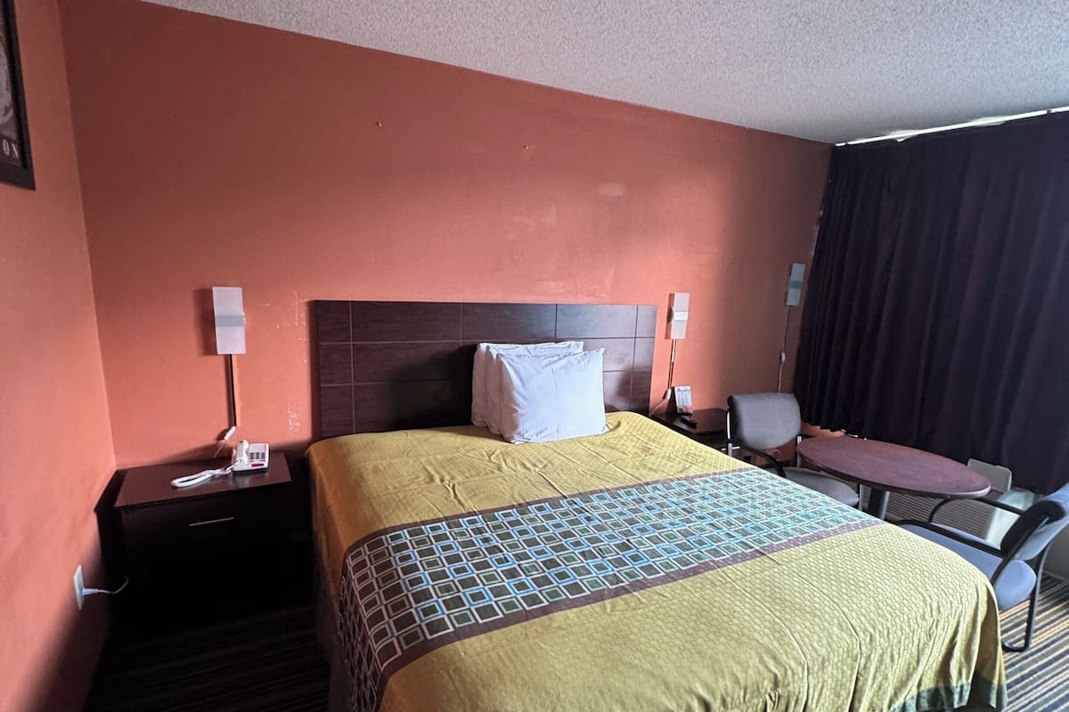 A hotel room with a large bed, a desk, and a chair. There is a telephone on the desk and a lamp on the nightstand.