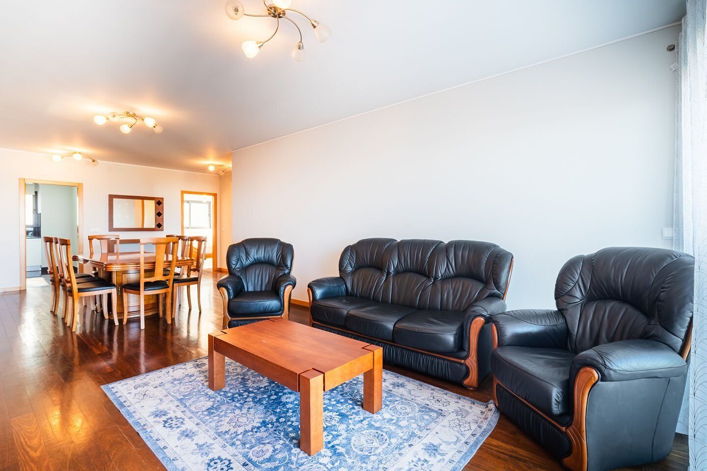 A living room with a wooden coffee table, black leather sofas, and a dining area with wooden chairs and a table.