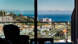 A view through a window of a coastal cityscape with buildings, roads, and a clear sky. - GuestReady - Homely stay in Funchal (Funchal)