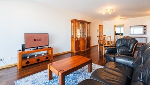 A modern living room with a flat-screen TV, wooden furniture, a glass cabinet, leather sofas, and a dining area. - GuestReady - Homely stay in Funchal (Funchal)