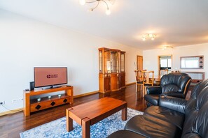 Una sala moderna con televisor de pantalla plana, muebles de madera, una vitrina de vidrio, sofás de cuero y un área de comedor.