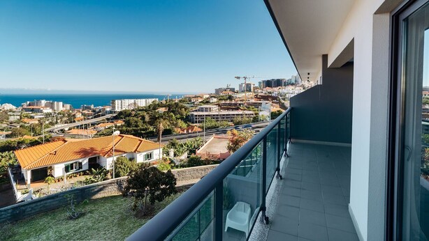 A balcony with a view of a coastal cityscape, including buildings and a clear blue sky. - GuestReady - Homely stay in Funchal (Funchal)
