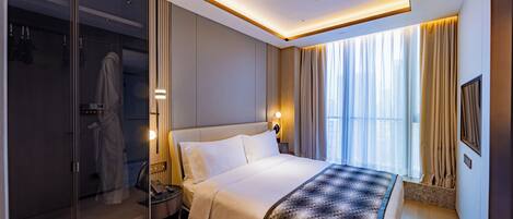 A modern hotel room with a large bed, a walk-in closet, and a bathroom with a glass partition.