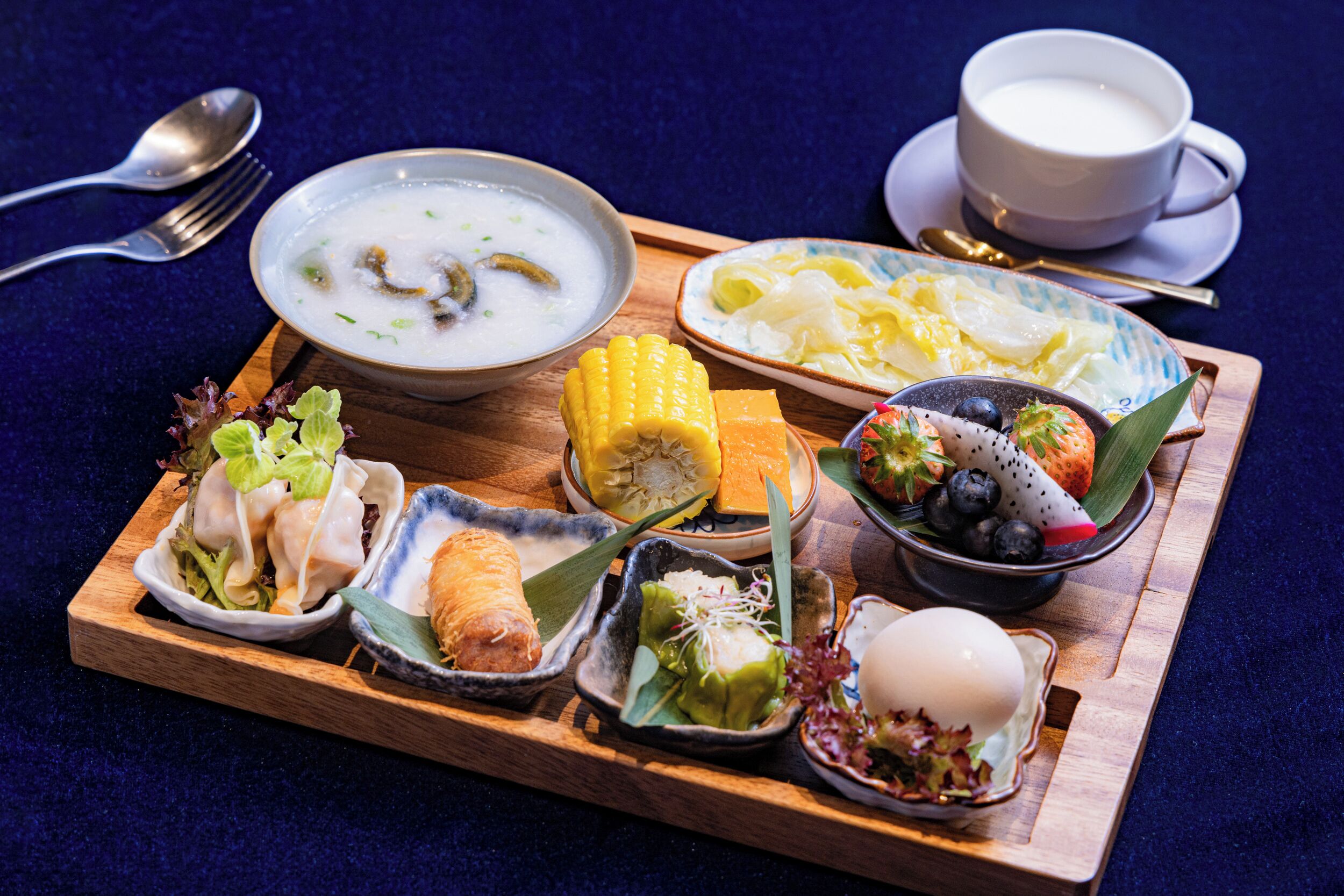 A wooden tray with various dishes including soup, corn, eggs, and vegetables.
