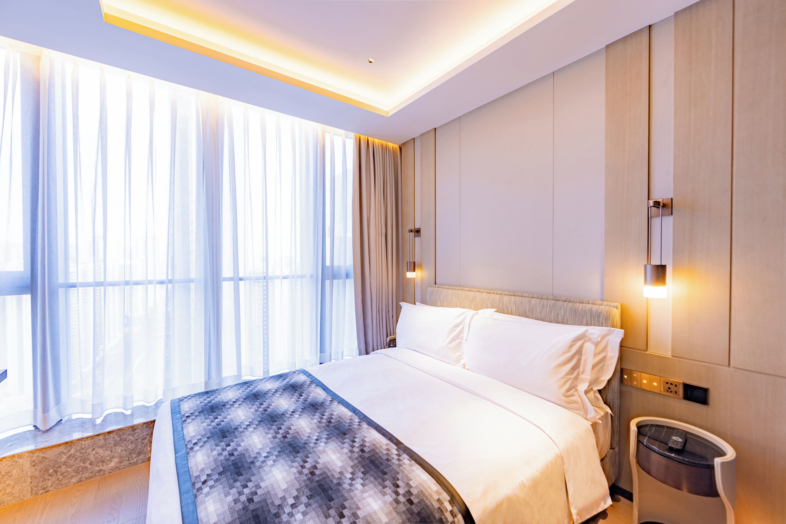 A modern hotel room with a large bed, a bedside table, and a nightstand.
