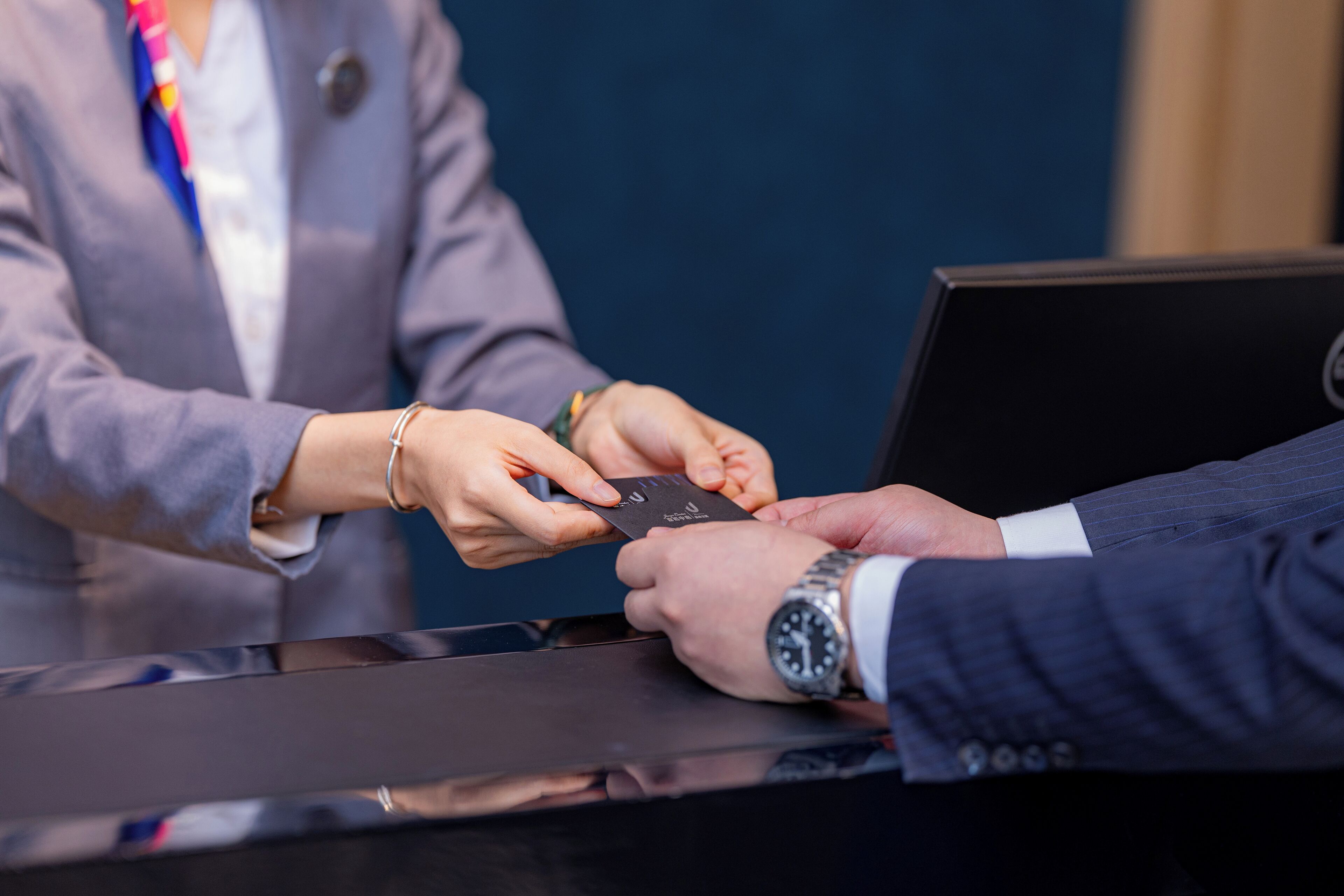 A person handing over a card to another person at a desk.