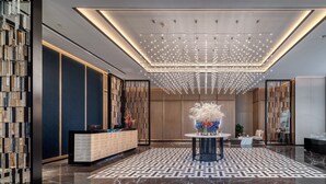 Een moderne hotellobby met een vloer met geometrisch patroon, een receptiebalie en een decoratieve kroonluchter.