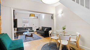 Ett modernt vardagsrum med en soffa, ett matbord i glas med stolar, ett soffbord och en trappa.