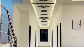 Un pasillo con un diseño moderno en el techo, una escalera a la izquierda y una silla azul oscuro a la derecha.
