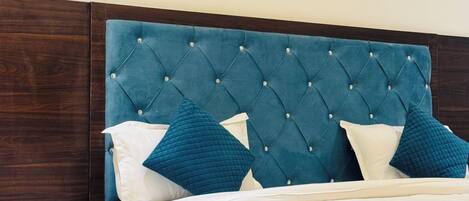 A bedroom with a tufted headboard, white bedding, and teal pillows.