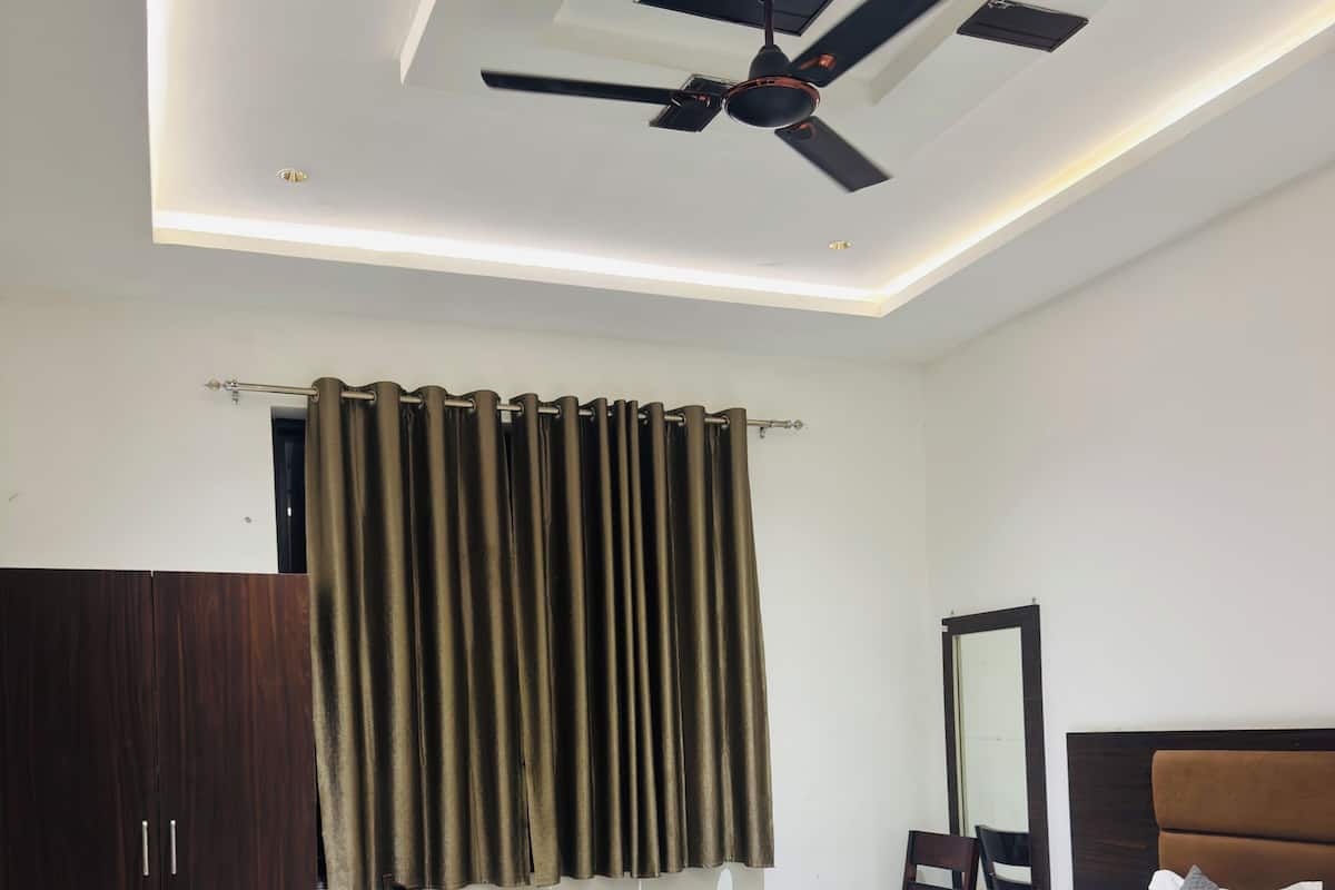 A hotel bedroom with a bed, a desk, a chair, a wardrobe, and a ceiling fan.