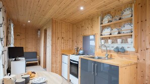 Un interior de madera acogedor, con una zona de cocina que incluye una estufa, un fregadero y estantes con vajilla.