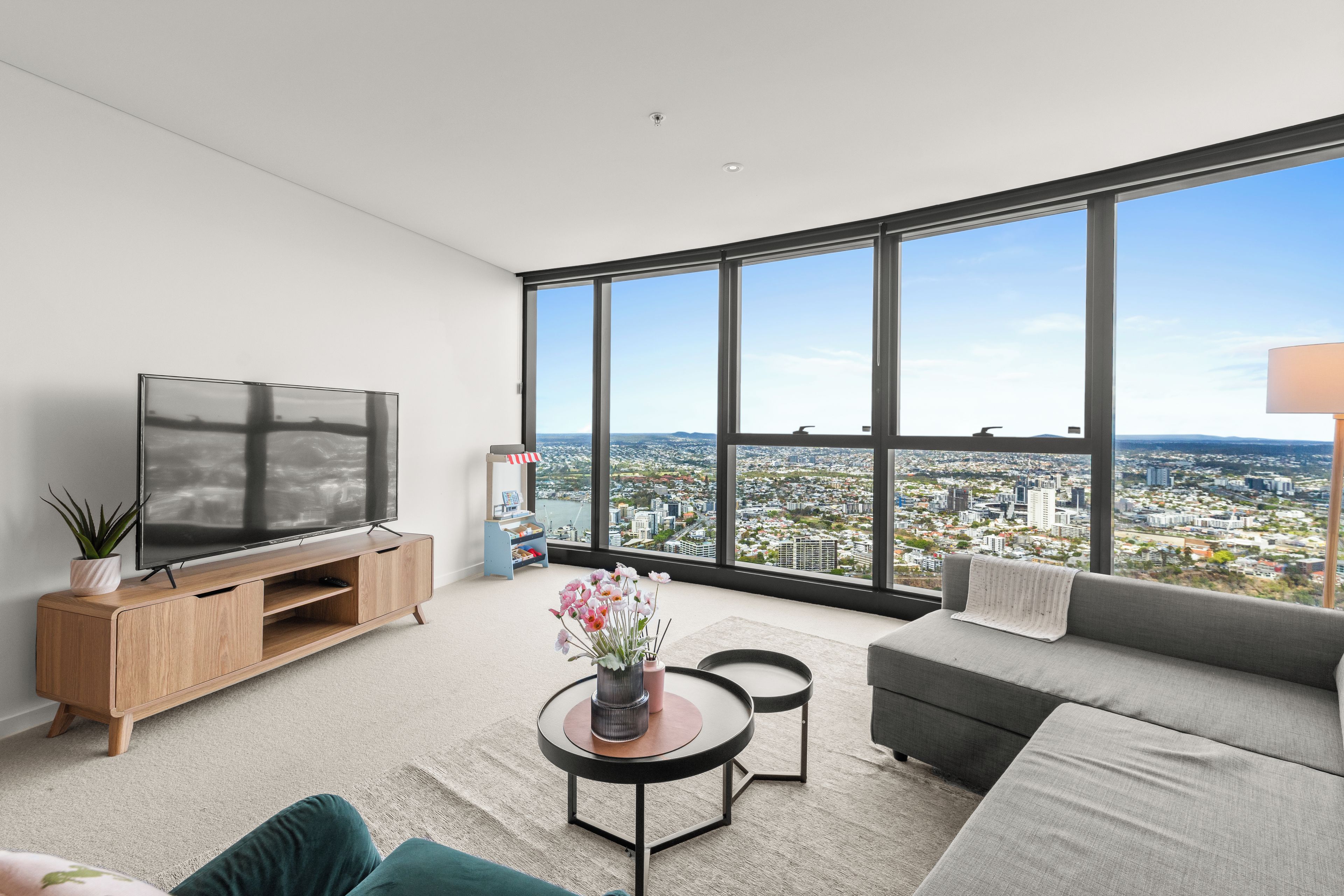 A modern living room with a large TV, a sofa, a coffee table, and a view of a cityscape through large windows.