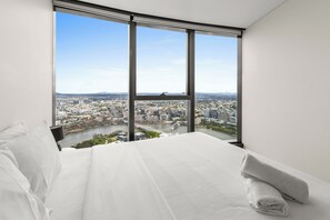 A bedroom with a large window, a bed, and a view of a cityscape.