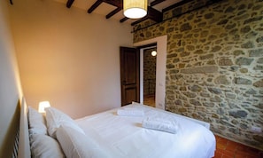 Un dormitorio con pared de piedra, puerta de madera y cama con ropa blanca.