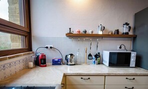 Une cuisine équipée d’une fenêtre, d’un four à micro-ondes, d’une bouilloire, d’une machine à café et d’une étagère contenant divers objets.