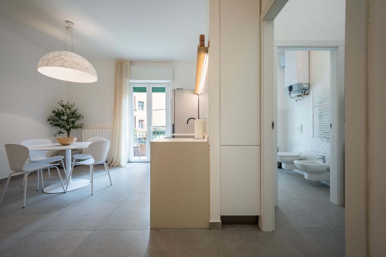 A modern kitchen with a central island, a dining area with a table and chairs, and a view of the outside balcony.