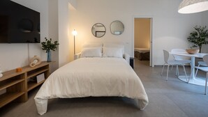 A modern bedroom with a large bed, bedside tables, a TV, and a dining area with chairs and a table. - Appartamento con balcone vicino a Castelvecchio (Verona)