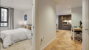 Ein modernes Schlafzimmer mit einem großen Bett, einem Schreibtisch und einer Küchenzeile im angrenzenden Raum.