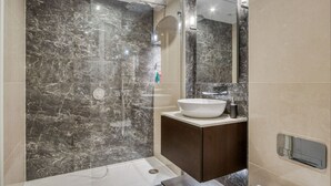 Ein modernes Badezimmer mit einer gläsernen Duschkabine, einem weißen Aufsatzwaschbecken und dunklen Marmorwänden.