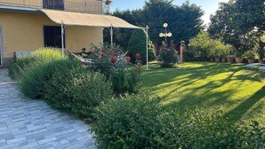 A two-story building with a covered patio, a lawn, and various plants.