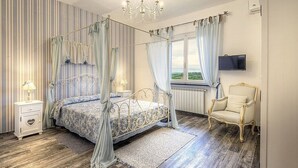 A four-poster bed with a canopy, a television mounted on the wall, a classic armchair, and a view of the outdoors through a window.