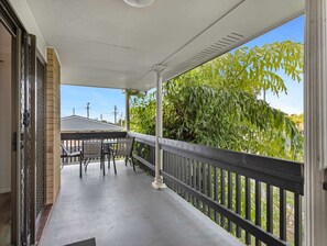 A covered outdoor area with a table and chairs, a railing, and a view of greenery. - Spacious 3-Bed Home with Balcony in Hervey Bay (Scarness)