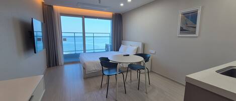 A hotel room with a bed, a dining table with chairs, a TV, and a view of the sea.