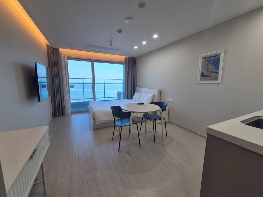 A hotel room with a bed, a dining table with chairs, a TV, and a view of the sea.
