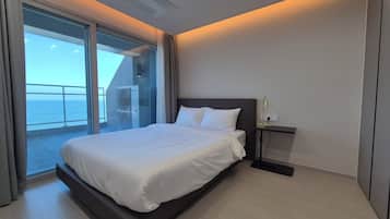 A modern hotel room with a large bed, a desk, and a view of the sea.