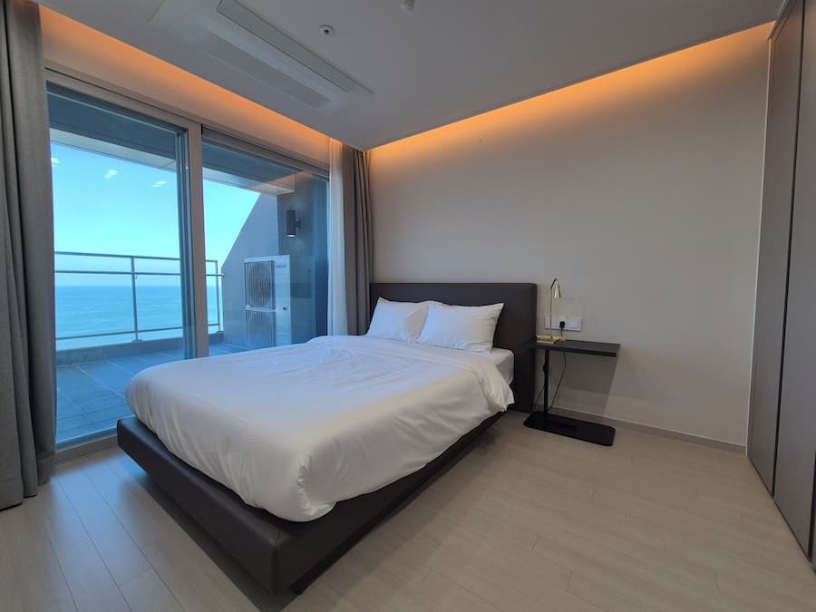 A modern hotel room with a large bed, a desk, and a view of the sea.