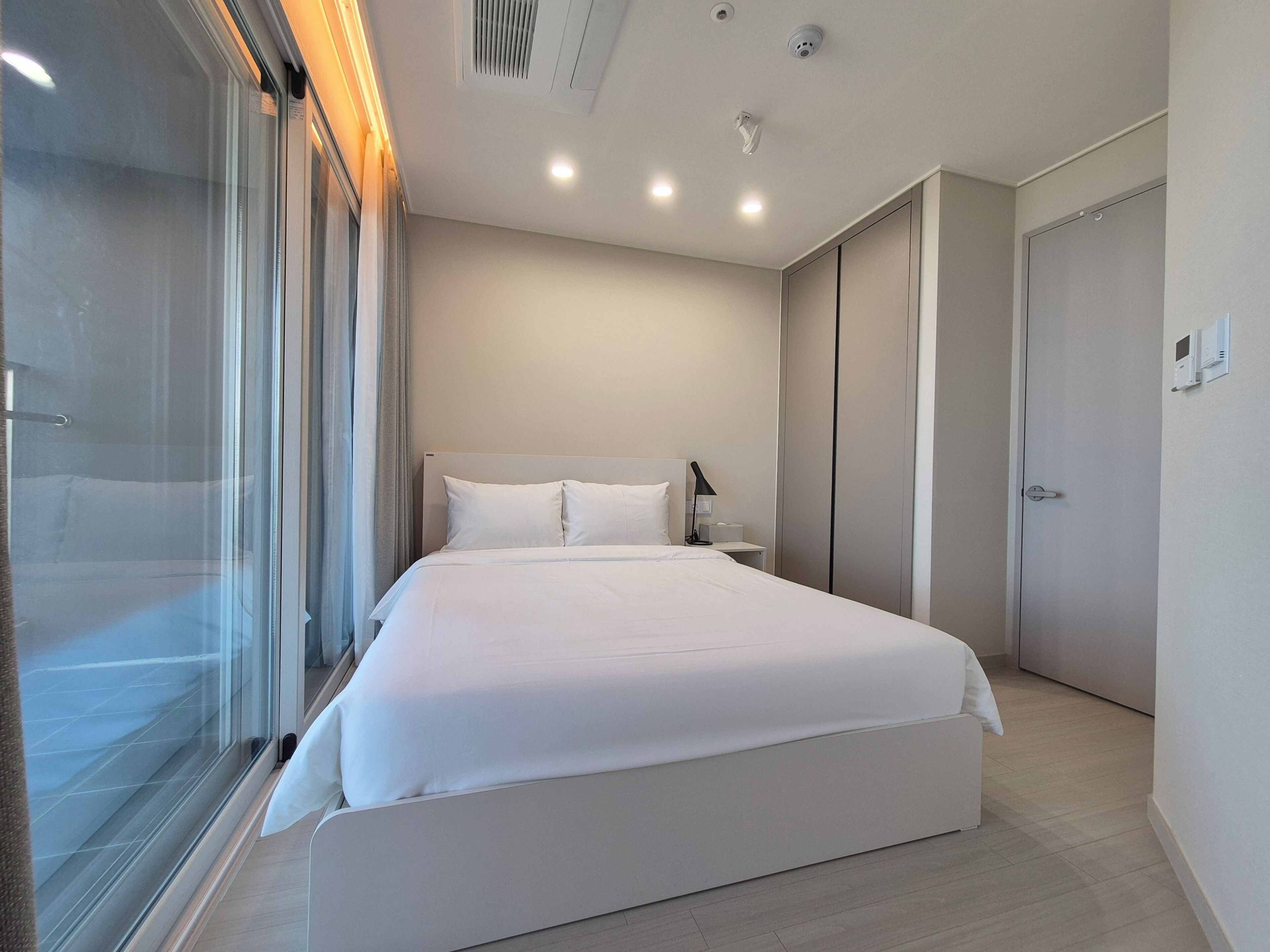 Una habitación de hotel moderna con una cama grande, una mesita de noche, una lámpara y un armario.