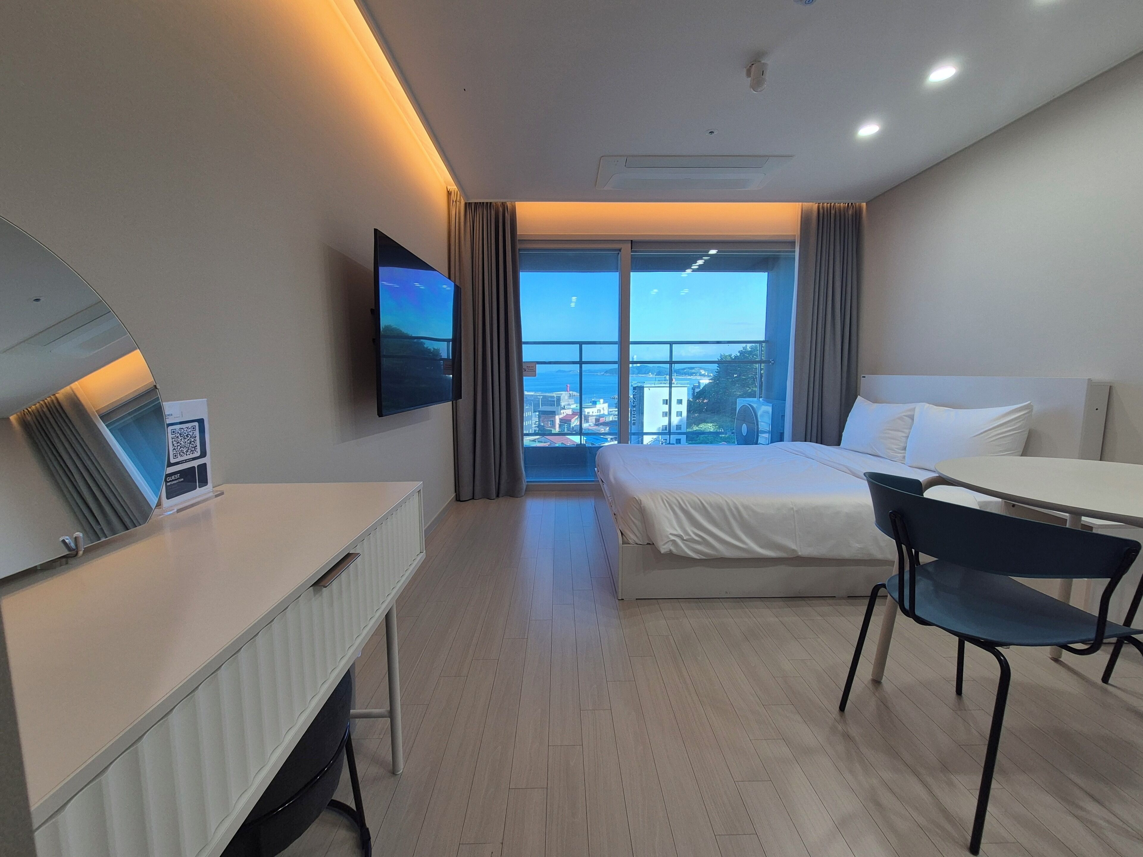 A hotel room with a bed, a desk, a chair, a TV, and a window with a city view.