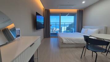 A hotel room with a bed, a desk, a chair, a TV, and a window with a city view.