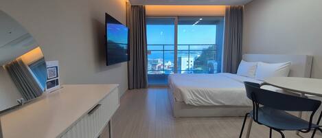 Habitación de hotel con cama, escritorio, silla, televisión y ventana con vista a la ciudad.