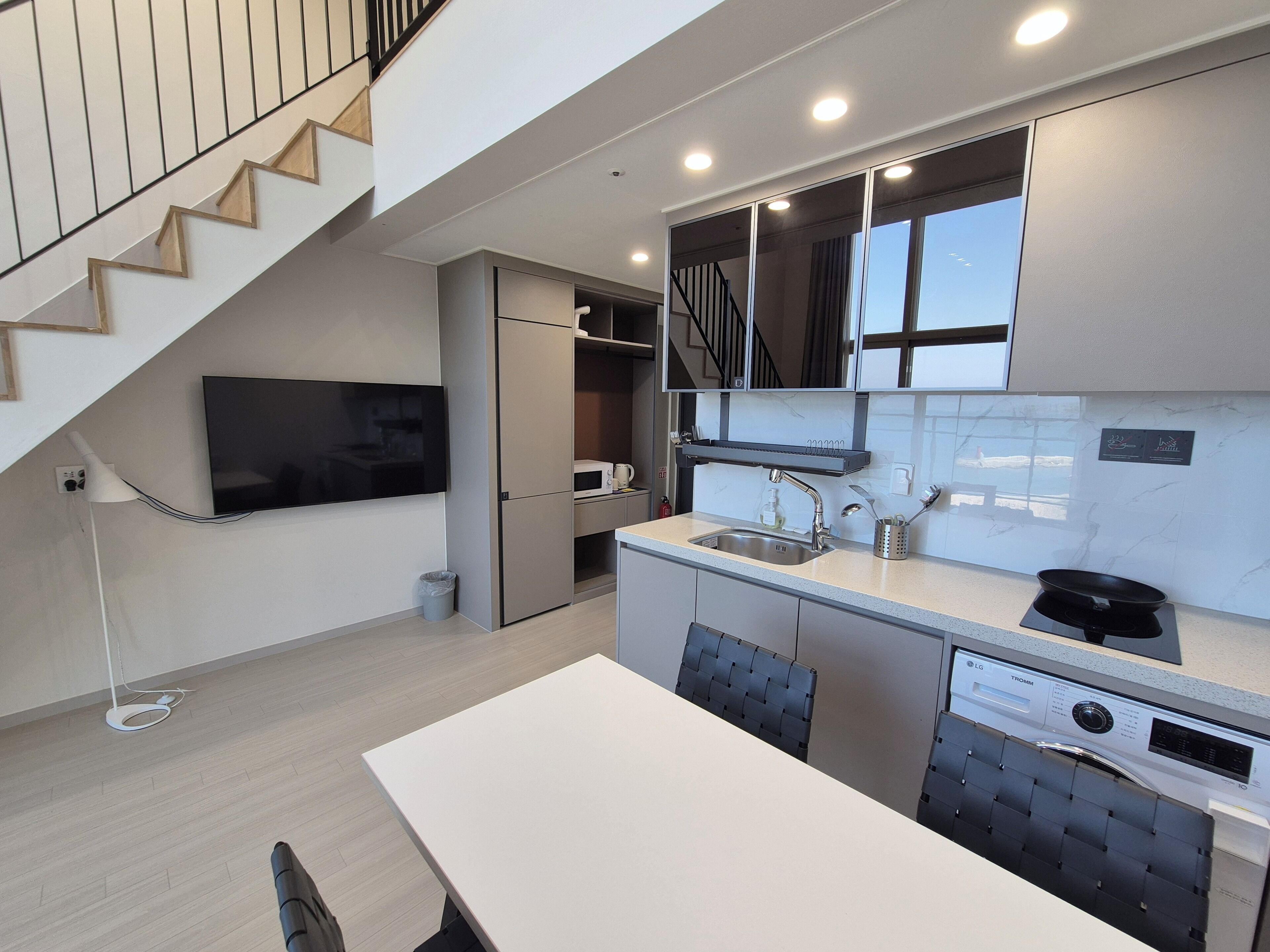 A modern kitchen with a built-in microwave, a sink, and a dishwasher. There is a staircase leading to an upper level.