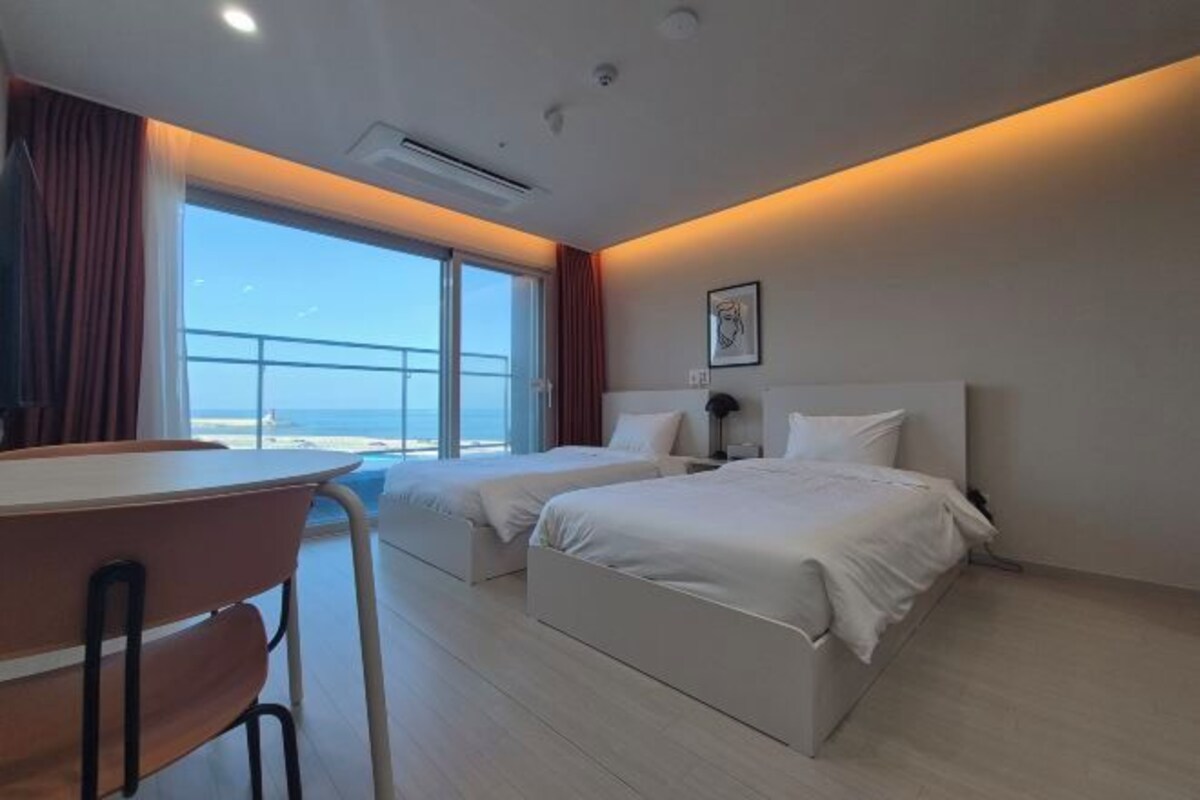 A hotel room with two beds, a desk, and a view of the beach.
